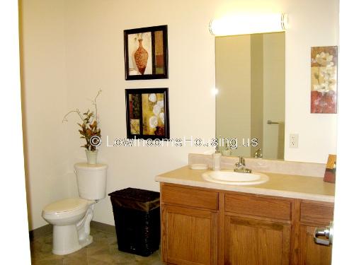 This is a photograph of a toilet room equipped with a toilet, a sink, a mirror, and storage areas for towels and sundries. 