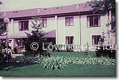 Photograph of two story row houses with installed awnings and beautifully maintained flower beds.  