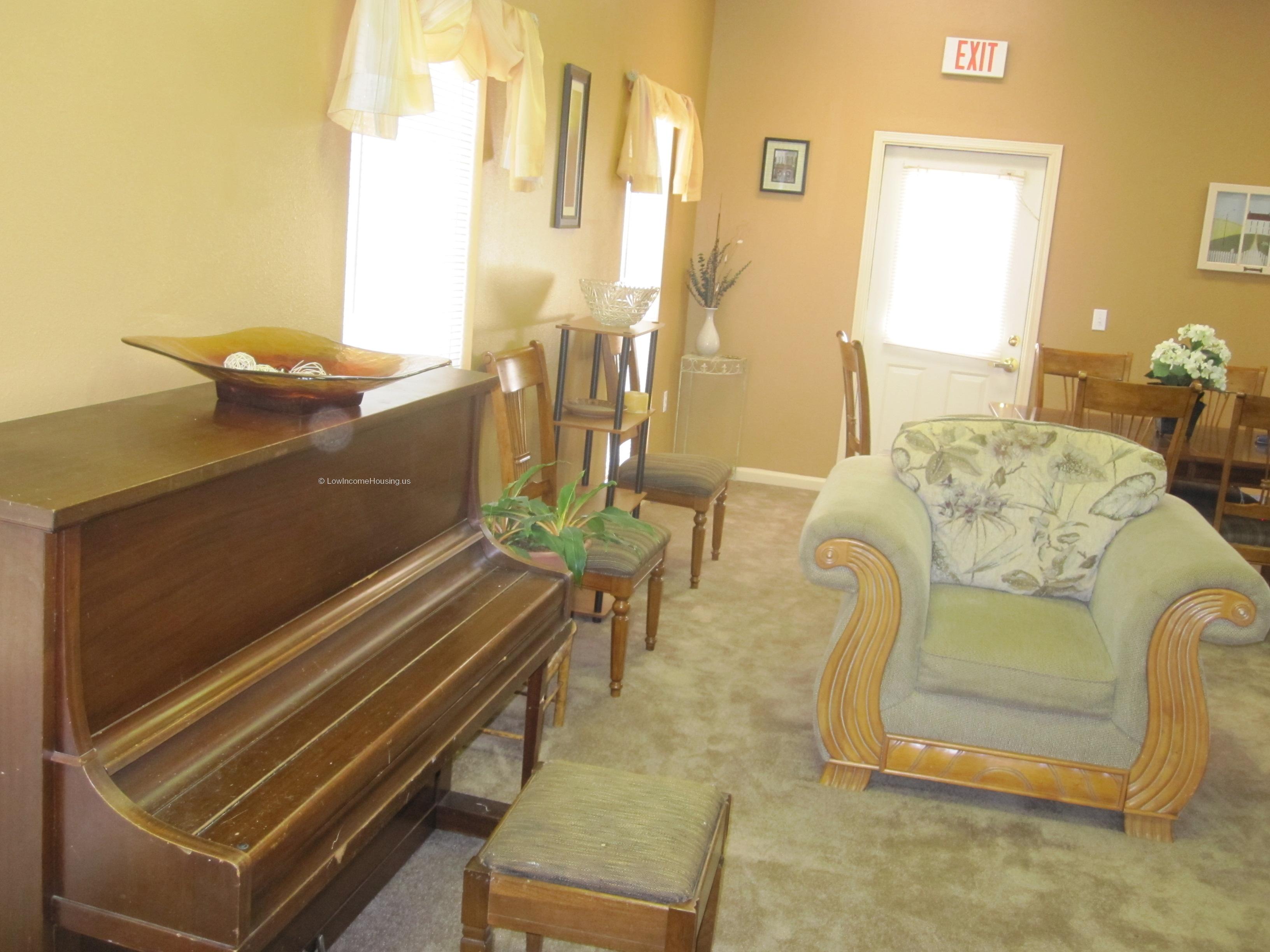 Classic upright piano, bright illumination, large overstuffed sofa with tasteful decoration and bright windows.
