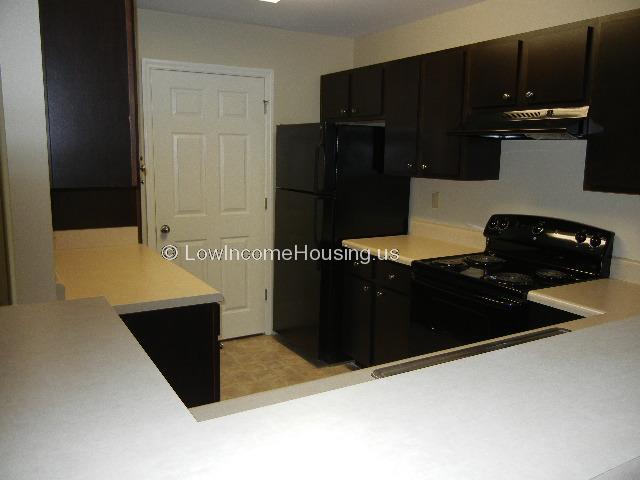Kitchen area with twin sink, stove with four burner units, refrigerator and cabinet storage.