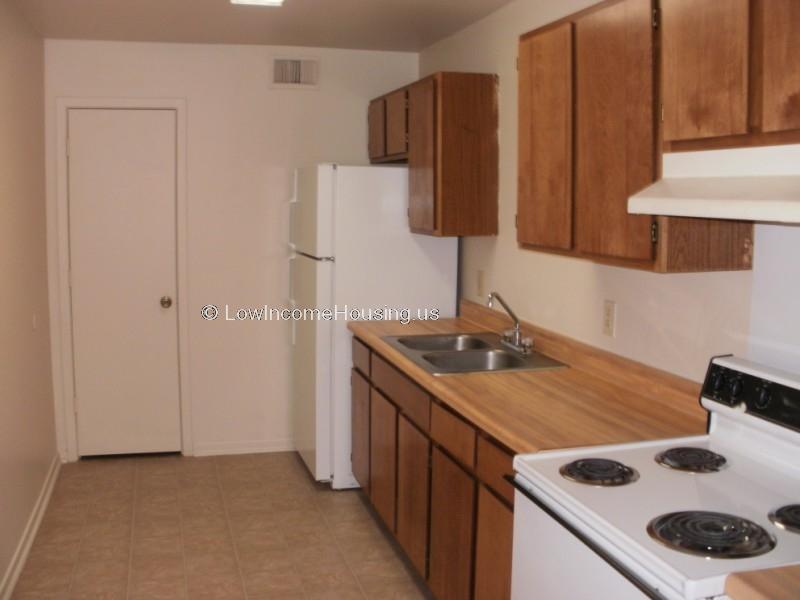 Interior view of fully equipped kitchen with refrigerator, freezer unit, stove with four burners, oven overhead exhaust fan and ample storage space.