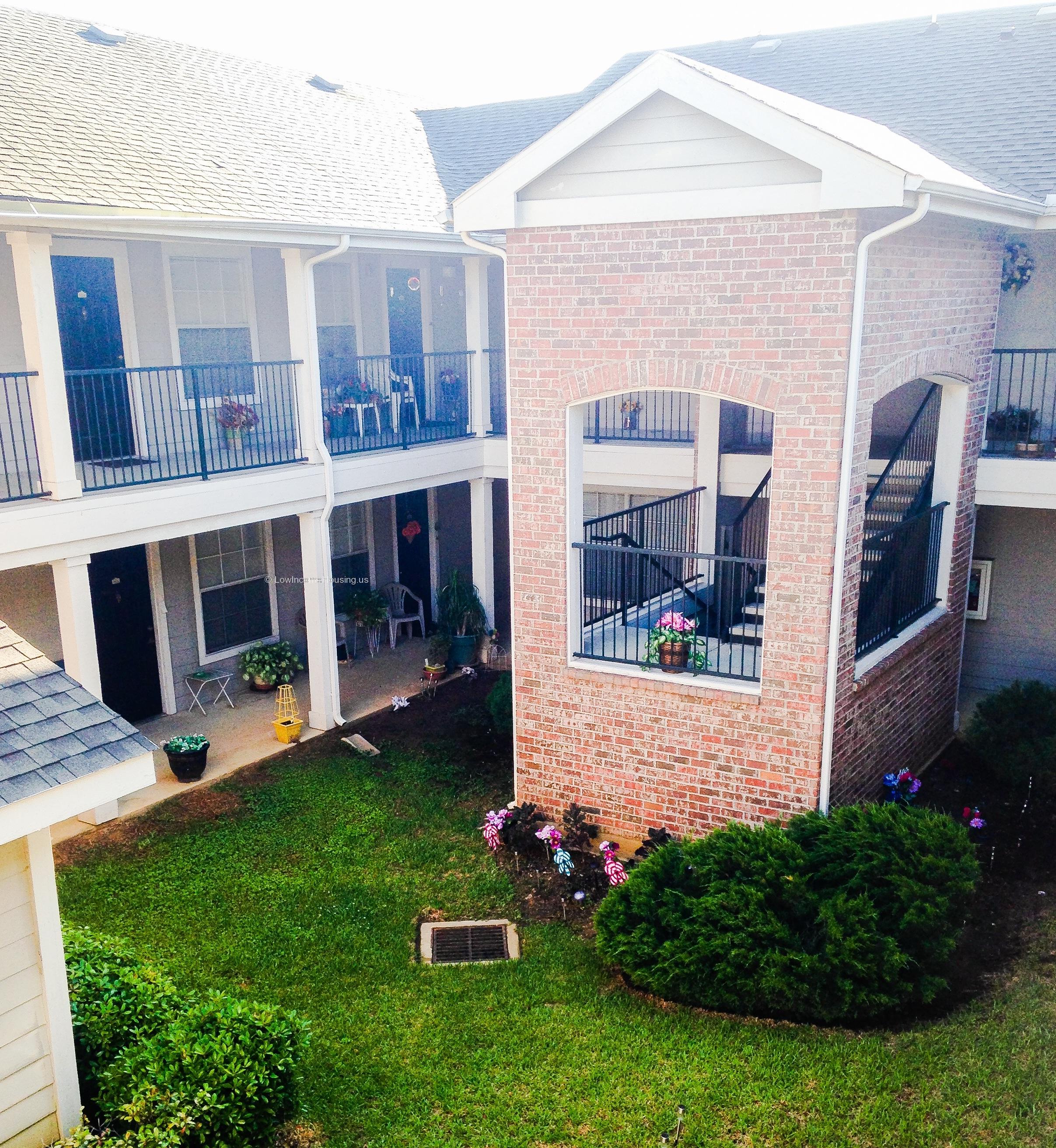 Interior view of apartment complex with several rooms, wrought iron railing and an ample number of potted plants.