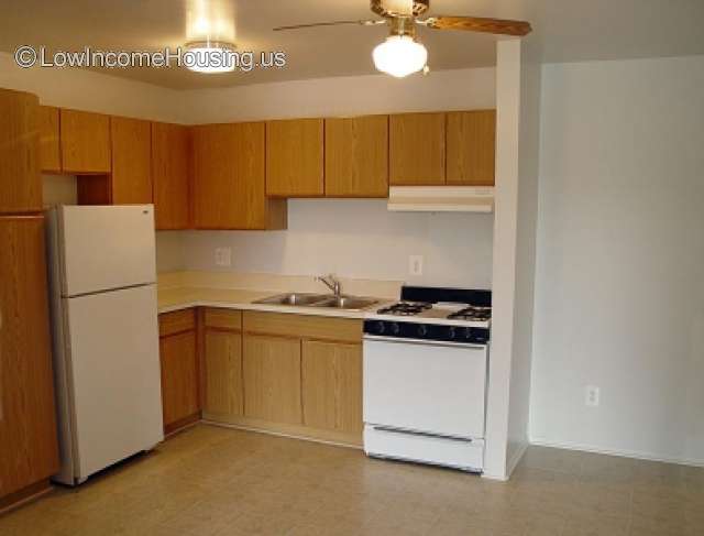 Interior view of kitchen unit equipped with twin sinks refrigerator freezer unit, oven with stove top burners and exhaust fan.