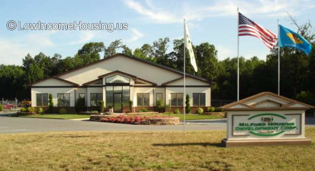 Streetview photo of main office building. Flag of the US, flag of Delaware, and a third flag. Driveway and sign of Milford Housing Development Corp.