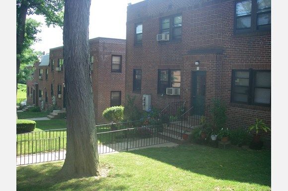 There are three large red brick buildings with window mounted air conditioners visible in all of the windows.  