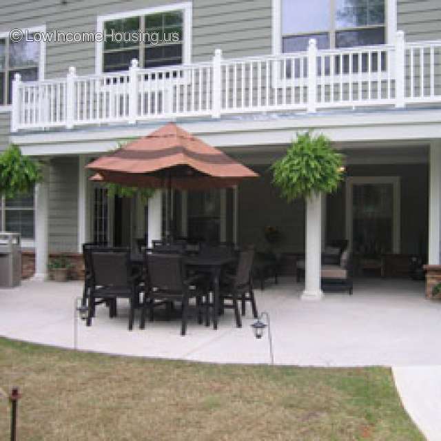 Exterior photograph of courtyard garden furniture, wooden table, various chairs, large Umbrella.  Items are located in courtyard setting.