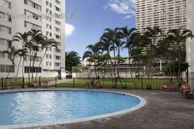 Large white multistory apartment building facing swimming pool with wrought iron fencing and lounge chairs 