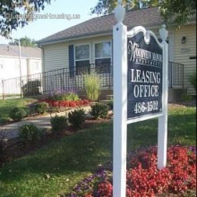 Housing unit with front entrance patio and two large dormer windows, wrought iron fencing and mature foliage in bloom. 