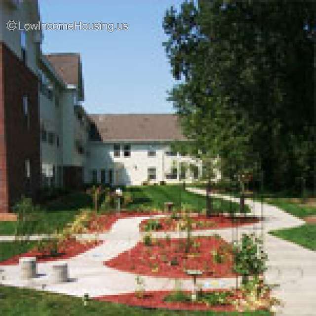 Courtyard with walkway. two and three story buildings. Trees on the right.