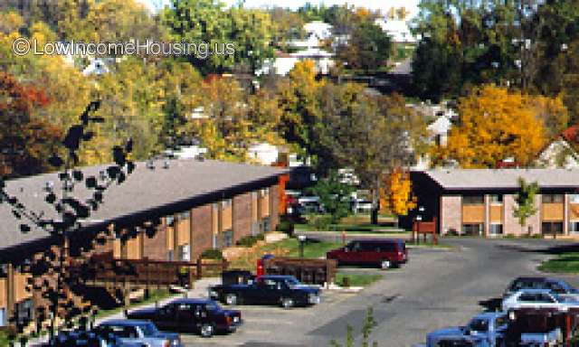 This is a photograph of Maple Hills Apartments.  It is a motel type of facility built in two levels.  There are a large number of automobiles parked in their parking lot.  