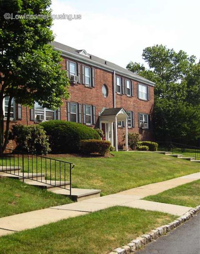 Streetview picture of two story townhouse red brick exterior. Sidewalk and four step entrance. Trees on both sides.