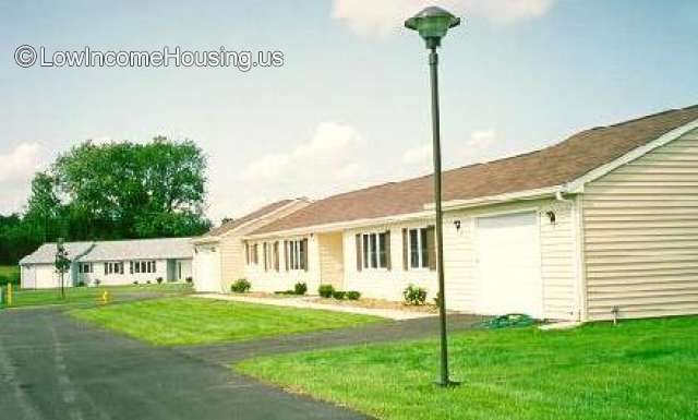 Street view of white vinyl siding one story homes.  A street light with round light in the grass.
