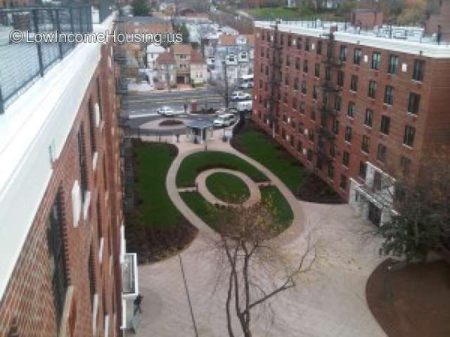 Area picture take from the roof top of a housing complex.  Two large red brick buildings which are six stories tall frame an open area.  There are six unit high and 14 units in length. 