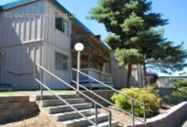 Two story housing unit with large windows facing parking area.  Ample foliage, mature trees. exposed balcony with sitting area overlooking resent parking.