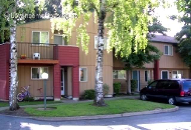 Large, three story housing unit with second floor balcony sitting area with entrance to unit, mature shade trees.