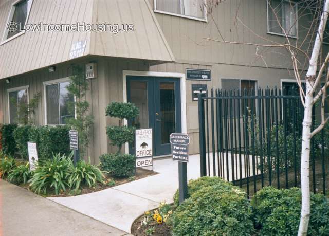 Picture of the front office with sign saying future resident parking, some bushes and a green fence.