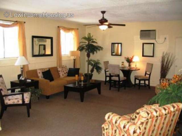 Indoor picture of living area a love seat, a coffee table, a sofa and a chair. Three framed mirrors hang on the walls and a AC unit above one of them. A ceiling fan and a small table with three chairs