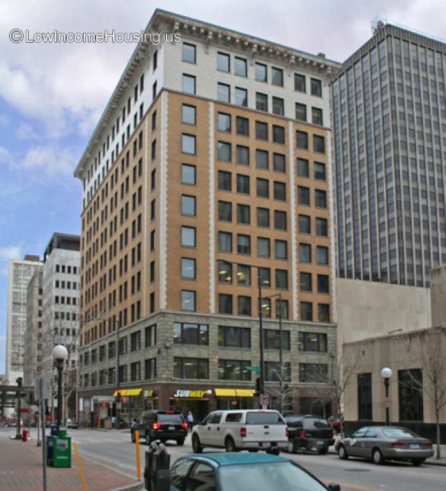 Steetview corner  picture from across the street of 12 story building in busy city. Cars driving by. Subway restaurant on ground floor.