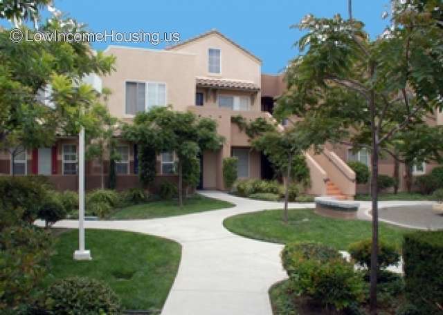 Outdoor photo of two story building. A exterior stair case leading from walkway. Lots of vegetation.