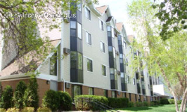 Outdoor photo of four story building. Lot's of windows. Trees on the right and hedges along side brick exterior