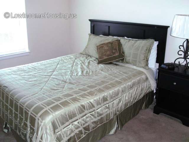 This is a photograph of what appears to be a king sized mattress on a bed frame.  A lamp can be see to the right of the bed. 