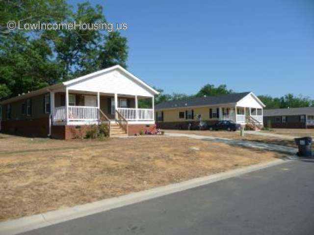 Large wooden frame structure which contains a covered porch.  There are wooden stairs leading up to the porch.  The stairs have hand rails on each side.  