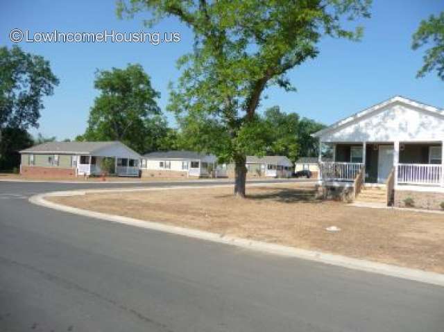 This photograph shows 5 housing structures which are very similar.  On the end of the building is a flight of stairs leading up to a porch. Each of the housing structure contains two windows on side. 