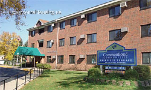 This is a photograph of FairField Terrace.  There is a large brick building that has air conditioning units installed next to each window.