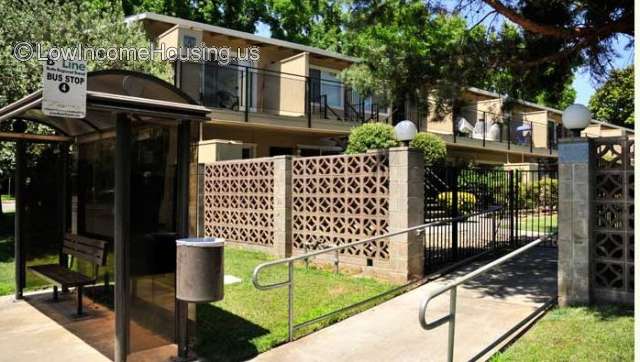 Photograph of six red brick town houses with fencing, enclosed bus stop and trash container. 