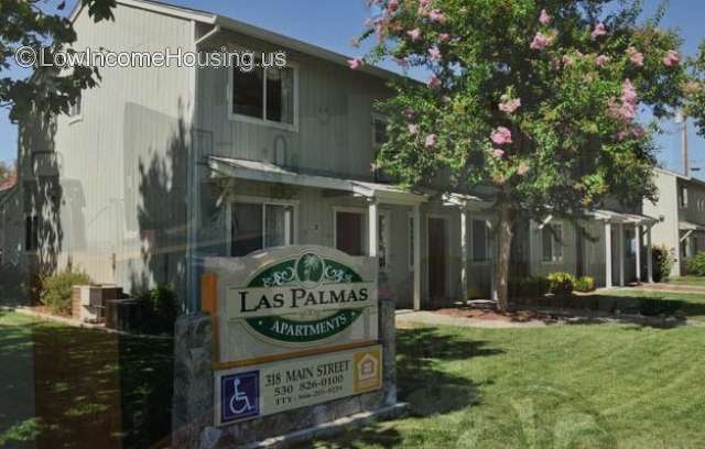 Las Palmas Apartments with photograph of two story housing unit, mature shade trees.
