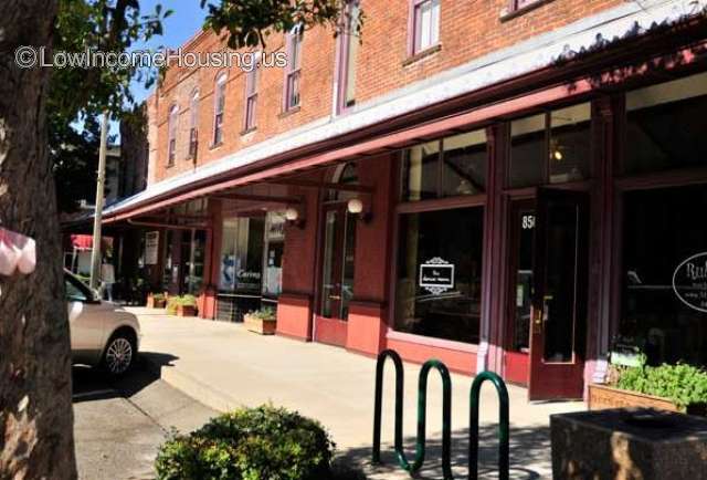 Red brick store front with variety of products available to purchase.  Ample sidewalk, Bicycle racks. Awning provides protection from the sun.  